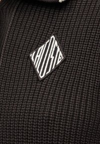 Tissu tricoté noir avec un patch losange blanc et noir comportant des rayures verticales et un motif d'éclair.