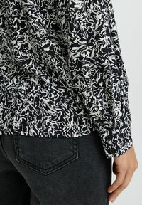 Camicia a maniche lunghe bianca e nera con un design a vortice testurizzato, dotata di polsini con bottone e indossata con jeans in denim scuro.