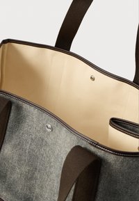 Γκρι τσάντα tote από ύφασμα με μπεζ εσωτερικό, σκούρους καφέ λαβές, επένδυση και κλείσιμο με κουμπί σνάπ, φαίνεται ανοιχτή από λοξή κορυφαία άποψη.