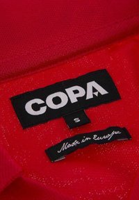 Rode stof met een gladde textuur. Heeft zwarte labels met de tekst "COPA" en "Made in Europe," met maat "S" op een ophanglus.