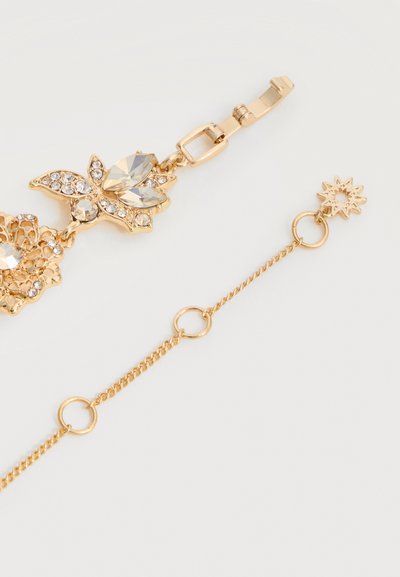 Zapestnica zlato barve z jasnimi kristalnimi obeski v obliki cvetlice in metulja, s verižico s krožnimi povezavami in sponko v obliki sonca.