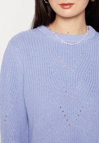 Suéter de punto de color púrpura claro con un patrón texturizado y recortes en forma de diamante. Cuello redondo y puños acanalados.