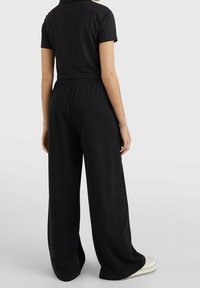 Černé kalhoty s širokými nohavicemi a elastickým pasem, vyrobené z měkké látky. Vyznačují se volným střihem a hladkou texturou.