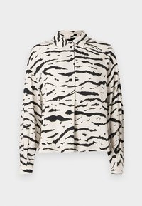 Chemise blanche à col avec un motif de rayures noires de tigre, manches longues, coupe décontractée, et fermeture boutonnée sur le devant. Texture de tissu douce.