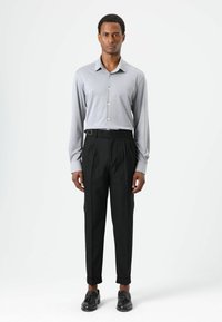 Grijs overhemd met lange mouwen en knopen, voorzien van een kraag, gecombineerd met zwarte geplooide broek met een broekriemlus en zwarte schoenen. Eenvoudige, op maat gemaakte pasvorm.