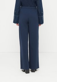 Παντελόνια με φαρδιά μπατζάκια από ύφασμα σκούρου ναυτικού χρώματος με απαλό υφή, διαθέτουν υψηλή ελαστική μέση και χωρίς ορατά σχέδια ή διακοσμήσεις.