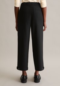 Schwarze weite Hosen mit elastischem Bund, mit einer Gesäßtasche und Druckknöpfen am Saum. Glatter Stoff.