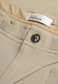 Beiga tygshorts med en texturerad yta, med knäppning, synlig sömnad och en etikett som säger "KAREN BY SIMONSEN."
