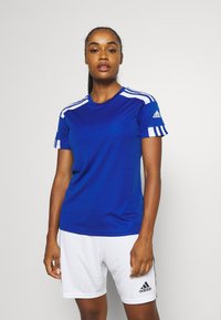 Camiseta deportiva azul con franjas blancas en las mangas, de cuello redondo, combinada con pantalones cortos blancos. Hecha de tejido transpirable, cuenta con el logo de Adidas en la manga.