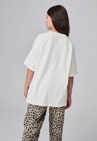Witte oversized T-shirt met korte mouwen en een losse pasvorm, gecombineerd met broek met luipaardprint in zwart en beige.