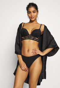 Svart lingeri-sett med polstret BH med blonde detaljer, glidelås foran og stroppe-design, kombinert med en matchende tanga. Satin svart kimono henger over skuldrene.