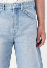 Jeans de denim azul claro con un corte relajado, que cuentan con cinco bolsillos, un cierre de botón y cremallera, y un sutil desvanecimiento en la tela.