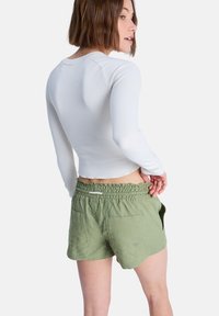 Chemise blanche à manches longues côtelée associée à un short en lin vert avec une taille élastique et deux poches arrière.