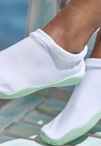 Chaussures d'eau blanches avec une texture lisse, semelles en caoutchouc vertes et un col flexible portant la marque "VENICE BEACH" en vert clair.