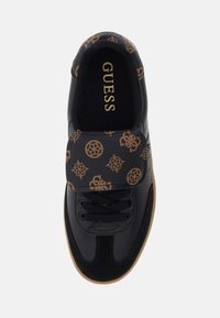 Tenis negri cu un exterior din piele texturată, având o curea cu model maro și sistem de închidere cu șireturi, precum și o talpă din cauciuc de tip gumă. Branding auriu „GUESS” în interior.