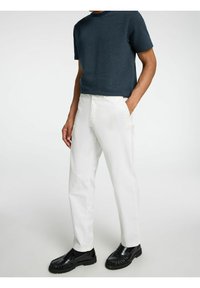 Witte rechte pijpenbroek gecombineerd met een gestructureerd marineblauw gestreept T-shirt. Zwarte instappers compleet met de outfit.