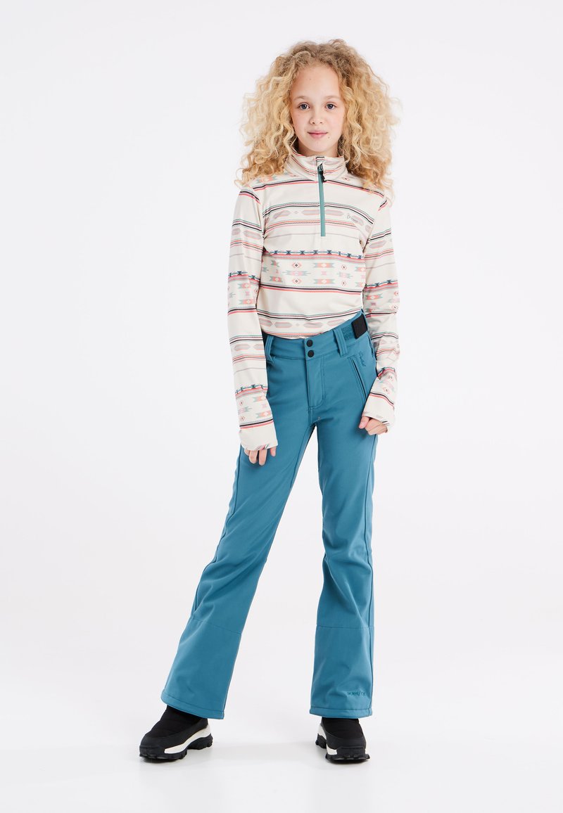 Maglione a maniche lunghe con zip di colore crema e righe orizzontali multicolore. Pantaloni da sci blu con gamba larga, abbinati a stivali invernali neri.