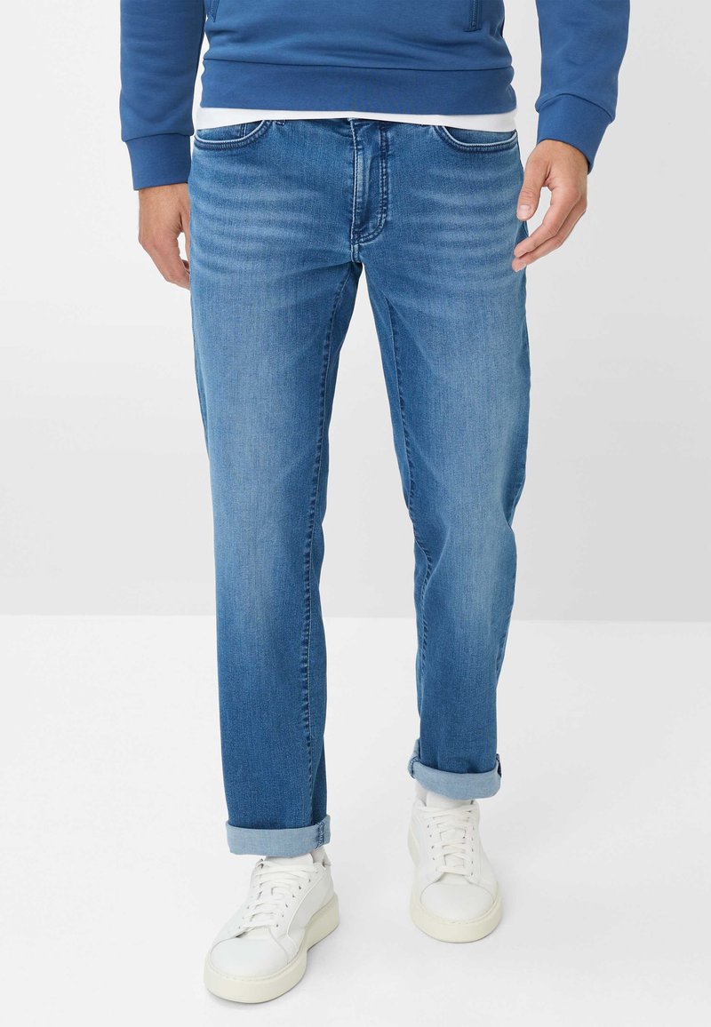Jeans in denim azzurro chiaro con taglio dritto, caratterizzati da dettagli sbiaditi, orli arrotolati e tasche anteriori. Abbinati a sneaker bianche.