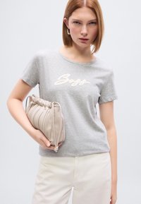 Γκρι κοντομάνικη μπλούζα με λευκό λογότυπο «Boss», σε συνδυασμό με μια μπεζ τσάντα φάκελο με υφή και σχεδιασμό με πιέτες.