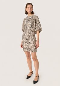 Leren mini-jurk met luipaardprint en pofmouwen, beige stof, aansluitende pasvorm, gecombineerd met zwarte spitse ballerina's en minimale accessoires.