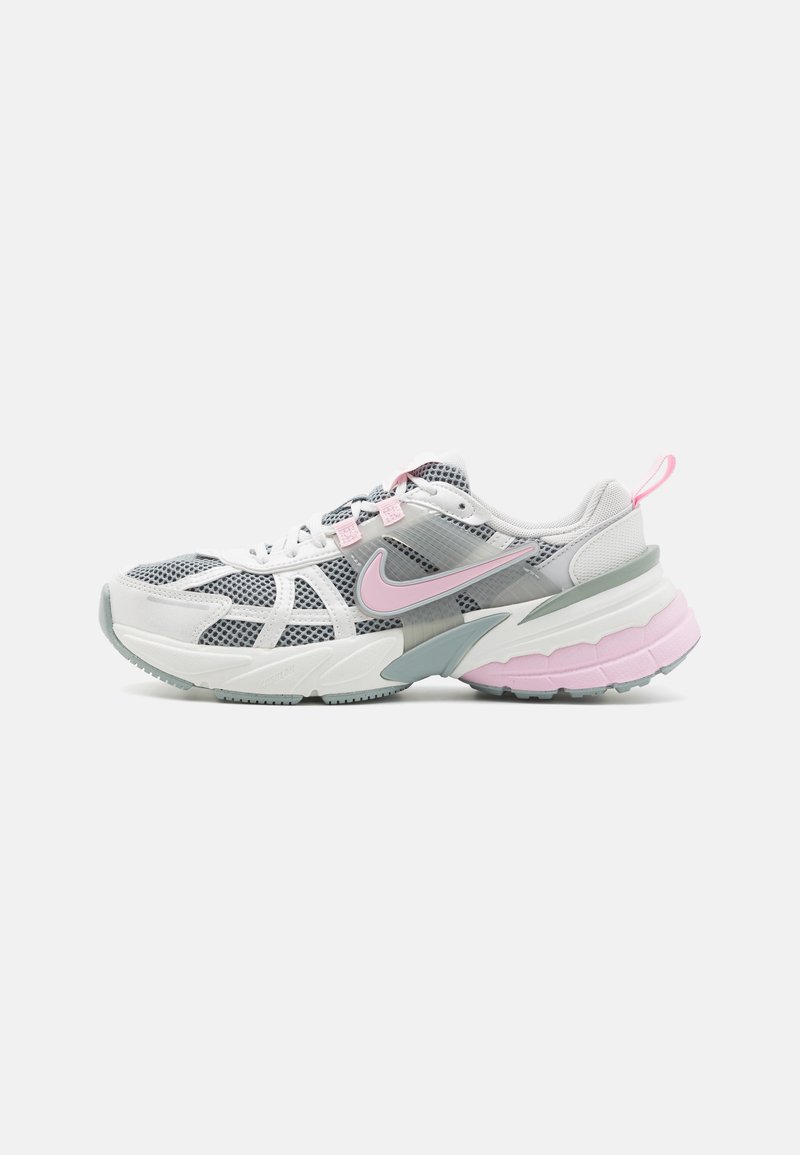 Zapatilla deportiva blanca y gris con parte superior de malla, acentos en rosa y una suela gruesa y texturizada. Presenta un diseño con patrón y una lengüeta.