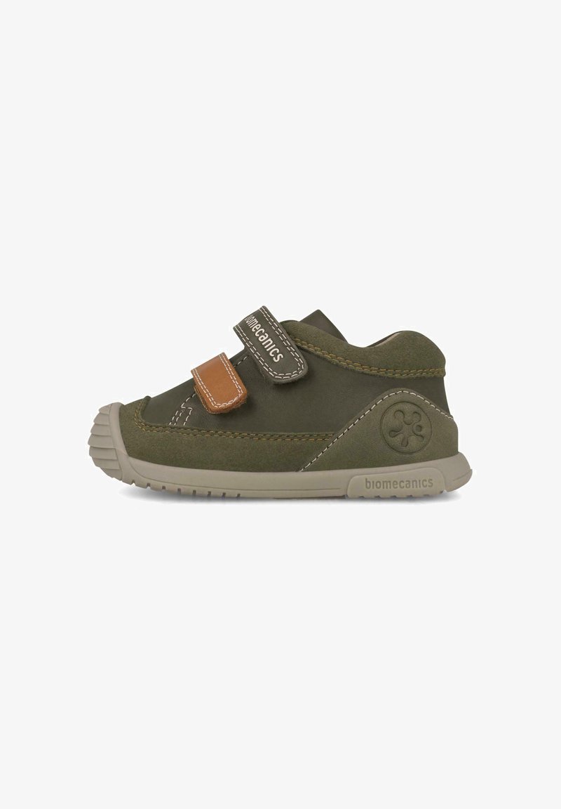 Zapato de cuero verde con punta redondeada, que cuenta con dos correas de Velcro y un acento marrón. Suela texturizada y logotipo de la marca en el lateral.