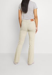 Beiga utsvängda byxor med bakfickor, en brun läderlapp på midjan och en mjuk bomullsmix. Bärs med en grå topp.