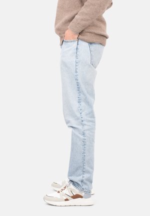 Jeans de color azul claro con corte slim y textura desvanecida, combinados con unas zapatillas deportivas blancas y grises con detalles en marrón.