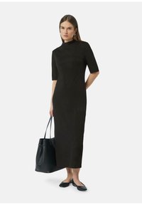 Robe noire midi à manches courtes et col montant, confectionnée en tissu lisse. Associée à un sac fourre-tout noir et des ballerines.