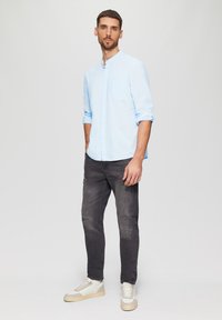 Lichtblauw overhemd met lange mouwen, met knoopkraag, gedragen met zwarte versleten jeans en witte sneakers met beige accenten. Eenvoudige, casual look.
