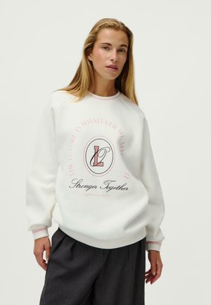 Biały sweatshirt z różowymi akcentami, z graficznym nadrukiem, który brzmi "Przyszłość to cokolwiek, co ją uczynimy" oraz "Silniejsi razem."