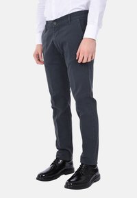 Pantaloni neri su misura con una texture liscia, due tasche frontali e chiusura con bottone, abbinati a scarpe eleganti nere lucide.
