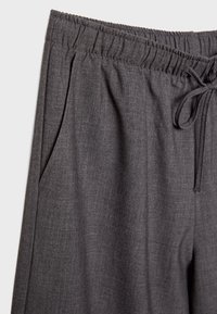 Gros plan sur un pantalon gris à taille élastique avec cordon de serrage et poche latérale, en tissu doux texturé.