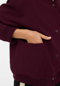 Giacca borgogna dal tessuto morbido, con taschino laterale e polsini a costine. Presenta chiusure a scatto e un design dal fit rilassato.