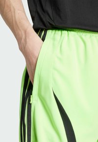 Neon green athletic shorts featuring a smooth texture, black accents, side pockets, and an elastic waistband for comfort and fit.