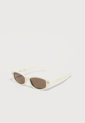 Lunettes de soleil blanches en forme d'œil de chat avec des verres foncés, petits logos dorés Medusa près des charnières, et la marque « Versace » sur les branches.