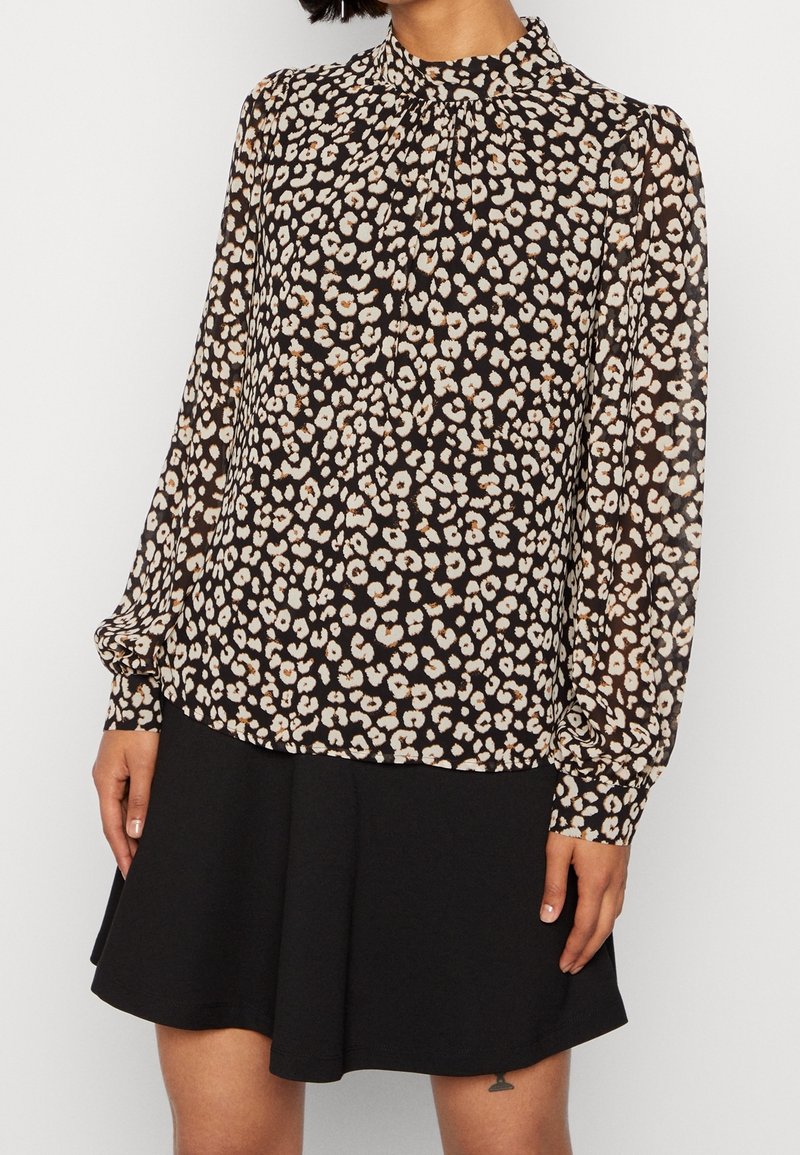 Schwarz-creamfarbige Leopardenmuster-Bluse mit hohem Kragen, langen Ärmeln und gerafftem Detail am Hals. Kombination mit einem schwarzen, ausgestellten Rock.
