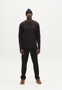 Svart långärmad tröja och matchande byxor med ribbat mönster. Modellen bär en svart stickad mössa och brun läderskor.