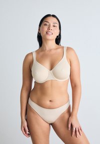 Beige-bh med en glatt tyg, strukturerade kupor och breda axelband som matchas med bikinitrosor. Enkelt design och sömlös textur.