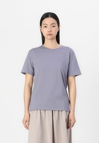 T-shirt kratkih rukava lavande boje napravljen od mekanog pamuka, s okruglim izrezom i malim logotipom na prsima, u kombinaciji sa svjetloplavi suknjom.