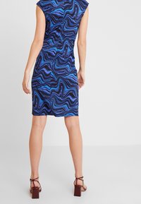 Blå och svart mönstrad klänning med vågig, abstrakt design; figurnära silhuett; korta ärmar; längd till mitten av låret; med bruna klacksandaler.