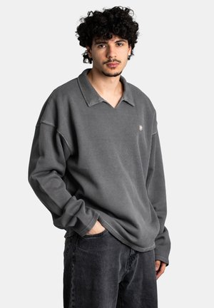 Gray ribbed pullover with a collar and a v-neck, featuring long sleeves. Paired with dark denim jeans, showing a relaxed fit.