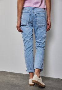Ljusblå denimjeans med avslappnad passform, uppvikt fåll och två bakfickor. Matchas med beige strukturerade skor, mot en neutral bakgrund.