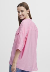 Camicia di tessuto rosa, stropicciata, con colletto, maniche corte e vestibilità rilassata. Presenta uno yoke posteriore e una tasca sul petto aperta e singola.