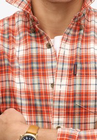 Camicia a quadri rossa e bianca con accenti blu e gialli, dotata di colletto classico e piccola etichetta con logo. Dettagli dei bottoni ben visibili.