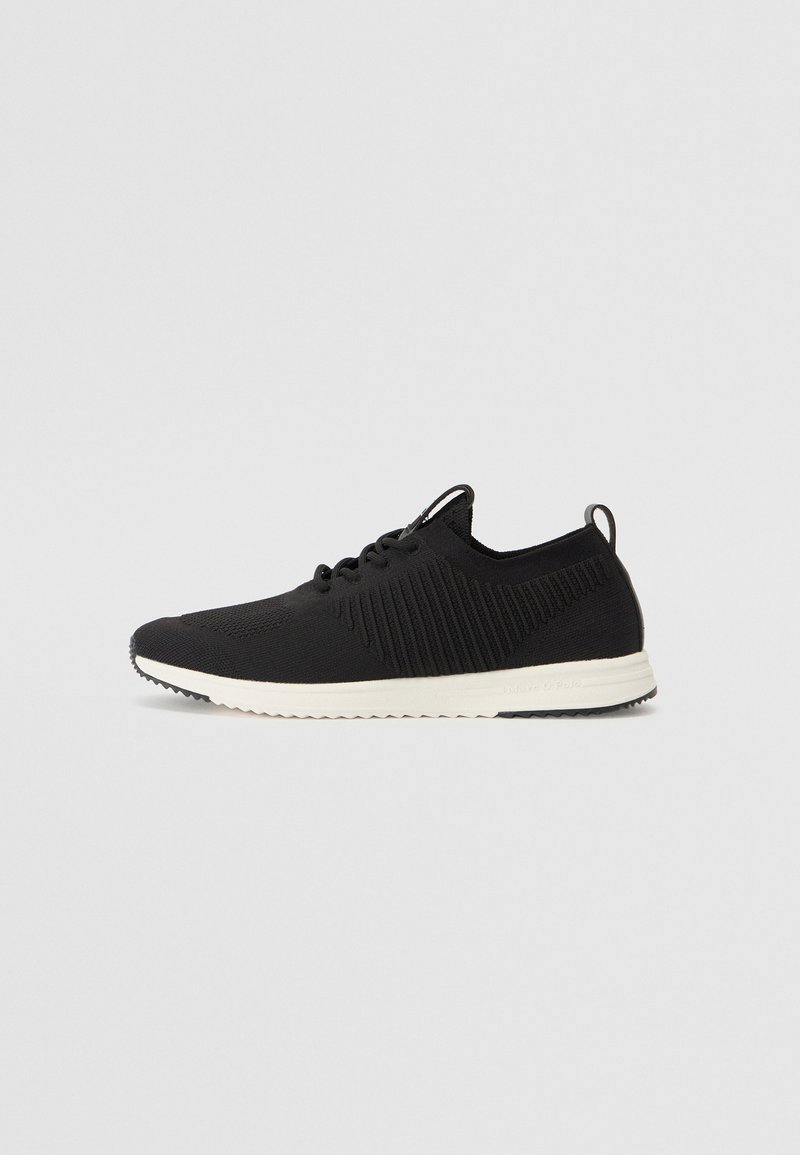 Sneaker noire avec un dessus en tricot texturé, semelle extérieure blanche, lacets et une languette au talon. Présente un design moderne et épuré.