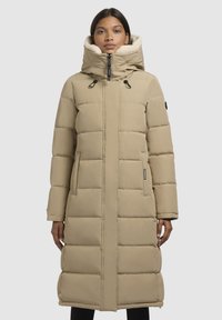 Bežs garš pūkains mētens ar kapuci, ar pāršūtu dizainu, divām sānu kabatām un melnu aparatūru. Mīkstais oderējums redzams apkārt kapucei.