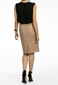 Blusa nera senza maniche con spalline arricciate abbinata a una gonna a tubino in pelle beige con spacco sul retro, indossata con sandali neri con tacco alto.
