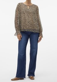 Blusa in stampa leopardata trasparente con scollatura a chiave e maniche a campana, abbinata a jeans a zampa d'elefante blu e scarpe basse beige.