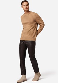 Lysbrun ribbet striktrøje parret med tætsiddende sorte læderbukser og beige ruskind chelsea støvler. Enkel, struktureret design og neutrale farver.